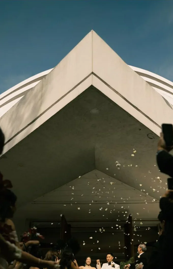 A couple walks out beneath angular architecture as petals fall.