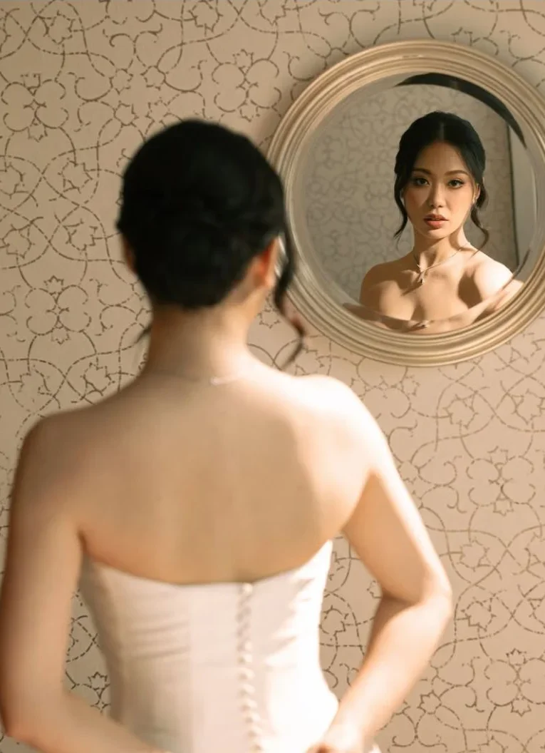 Bride seen from behind, her face reflected in a round mirror.
