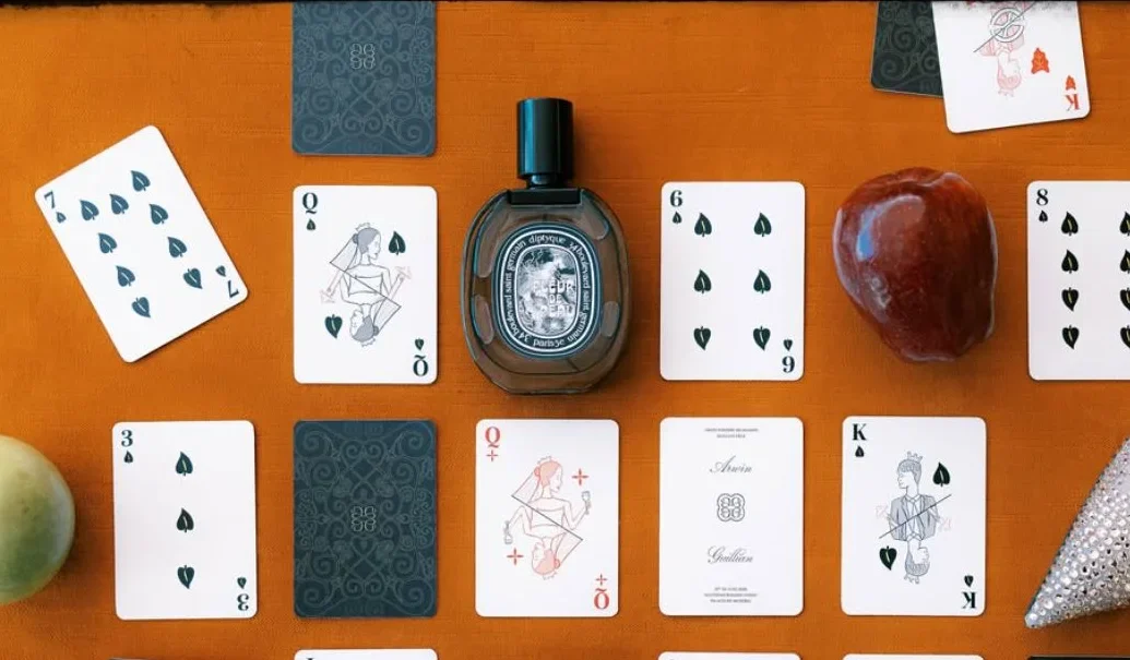 Playing cards and a perfume bottle arranged across an orange surface.