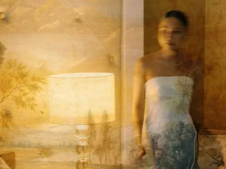 A bride stands near a glowing lamp in a layered, warm-toned photograph.