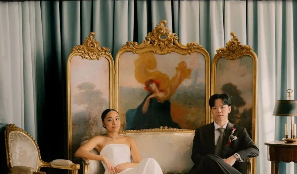 A couple sits beneath an ornate painted screen in a softly lit room.