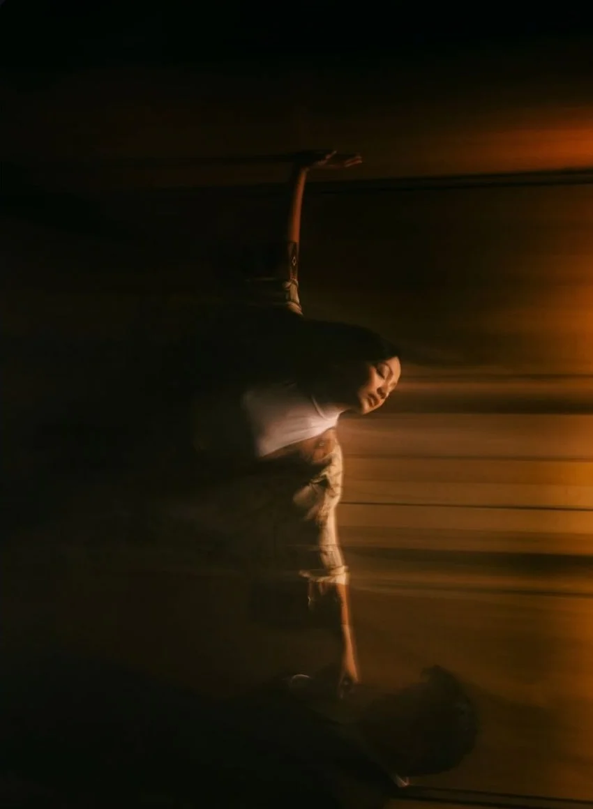 A dancer emerging from shadow into a narrow band of amber light.