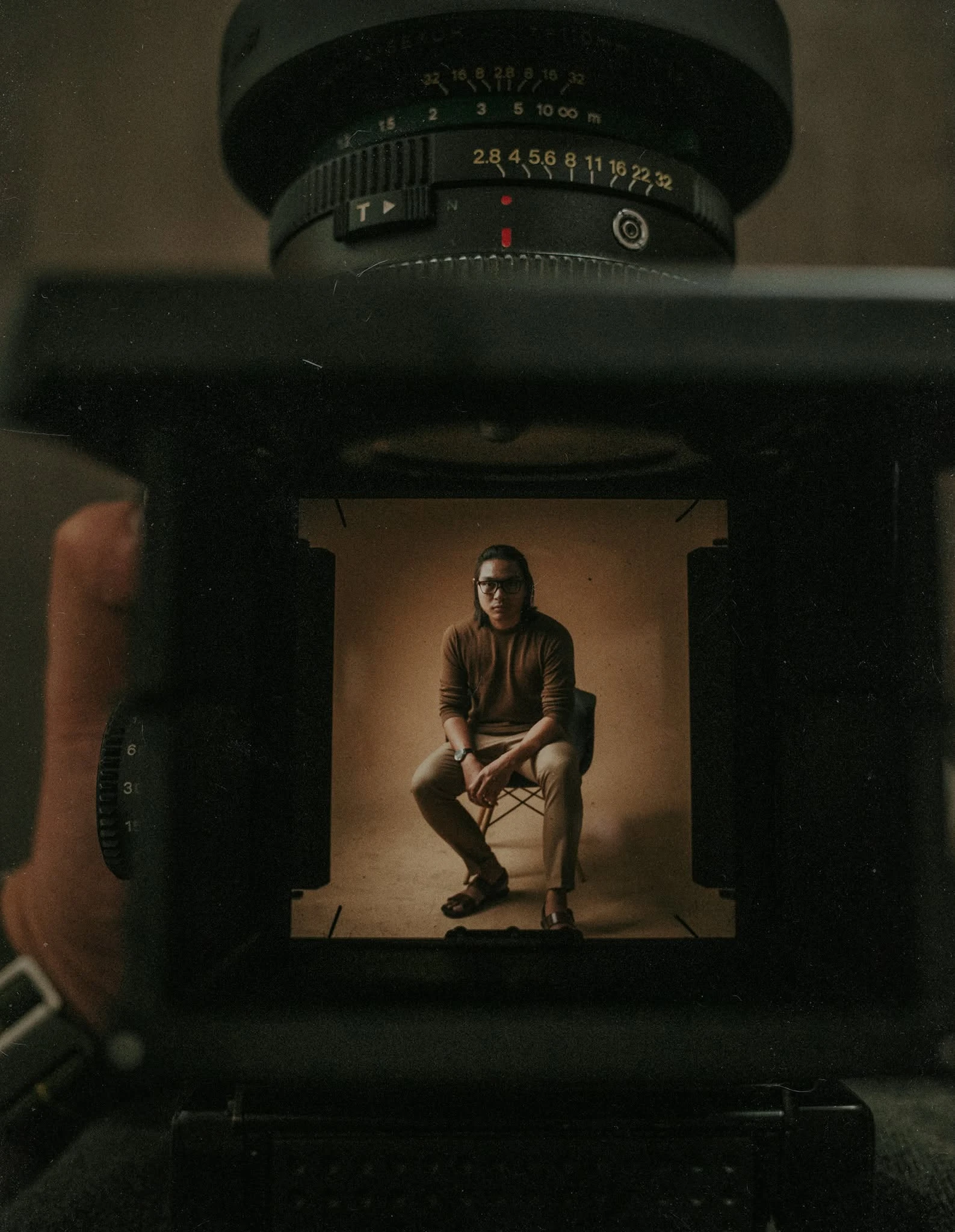 Mico Gonzales seated in a warm-toned portrait, seen through the frame of a camera