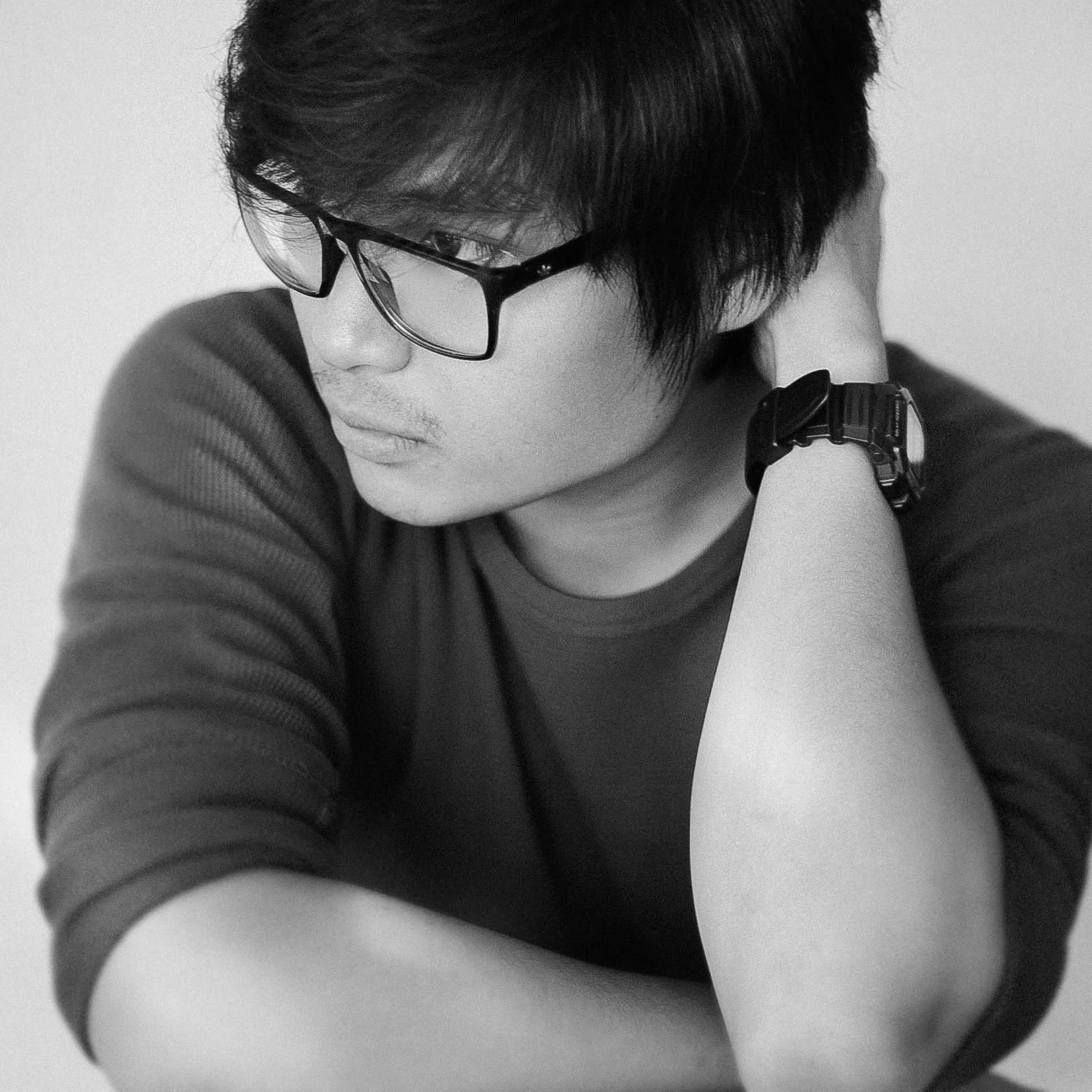 Black-and-white close portrait of Mico Gonzales wearing glasses, his hand resting behind his head
