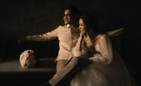 A couple seated together in a softly lit dark room